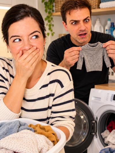 Couple doing laundry — man holding tiny shrunken sweater, woman covering her laugh — comedy sketch
